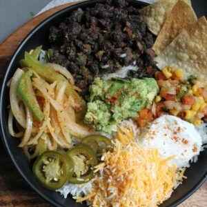 Colorful Mexican burrito bowl featuring guacamole, black beans, and shredded cheese.